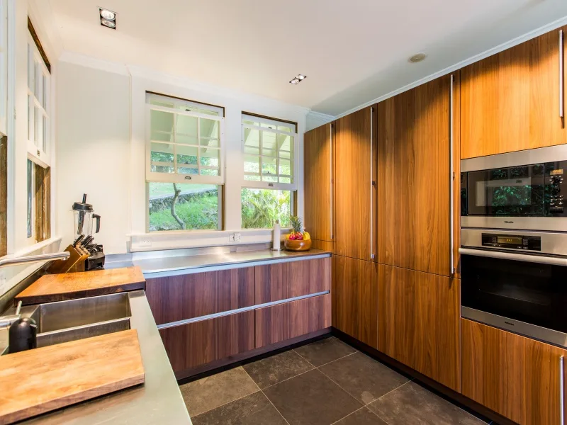 A modern kitchen with wood cabinetry, a central island, and windows overlooking greenery.