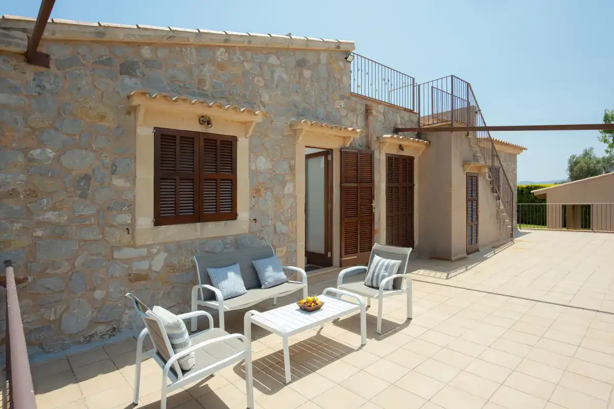 A stone house opens onto a sunny tiled terrace with outdoor seating.