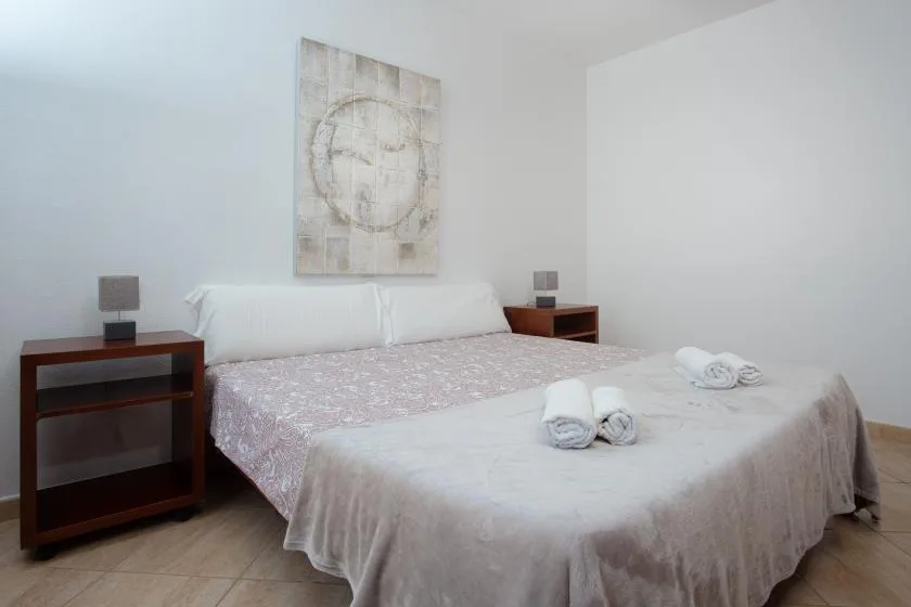 A bright bedroom with a bed, folded towels, and matching bedside tables.
