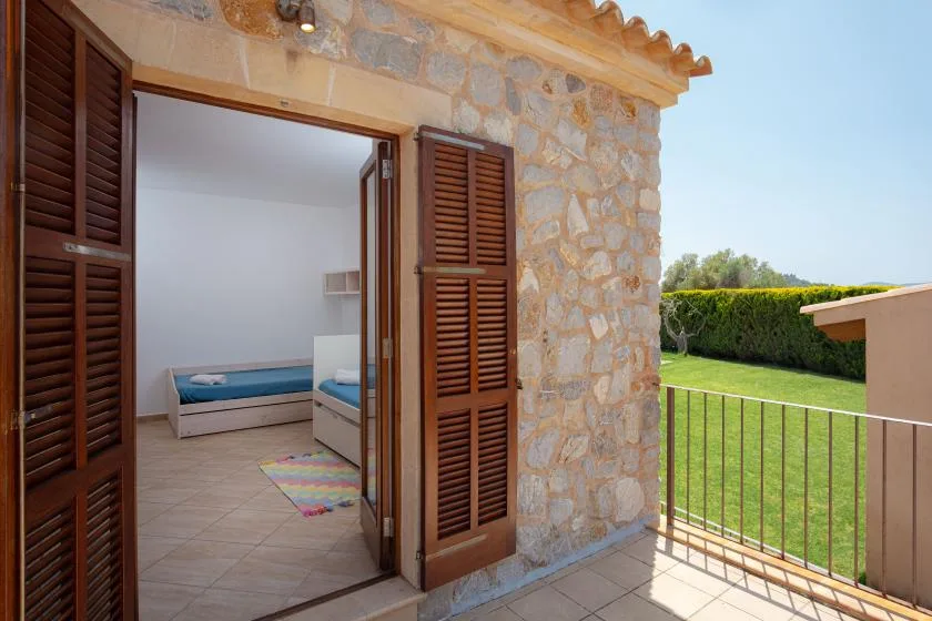 A stone patio with open wooden shutters overlooks a grassy garden.