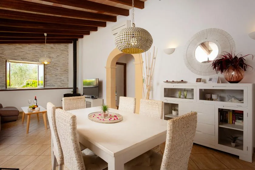 A bright dining room with a large table, woven seating, and a glass-front cabinet.