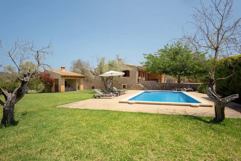 A swimming pool and seating area sit in a grassy garden beside a stone house.