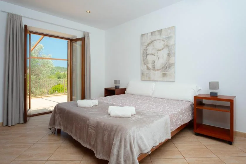 A bedroom with a double bed and an open window overlooking greenery.