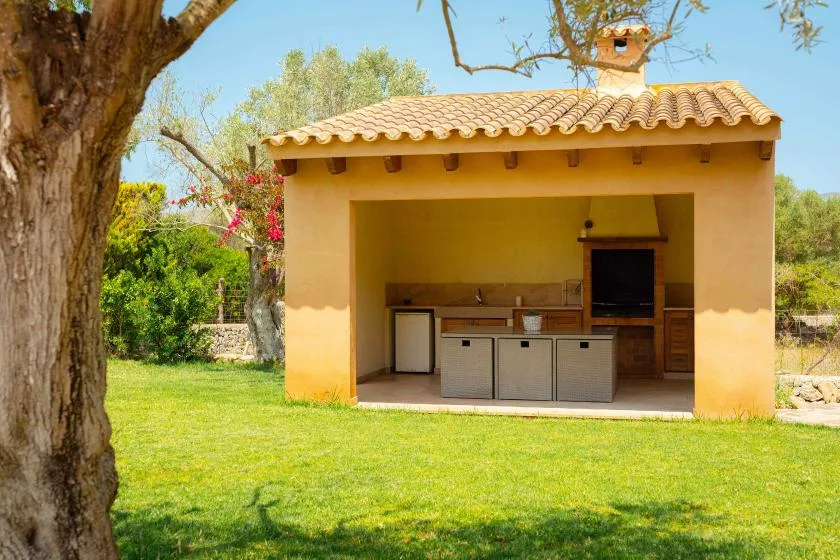 An outdoor kitchen beneath a tiled roof opens onto a green lawn.