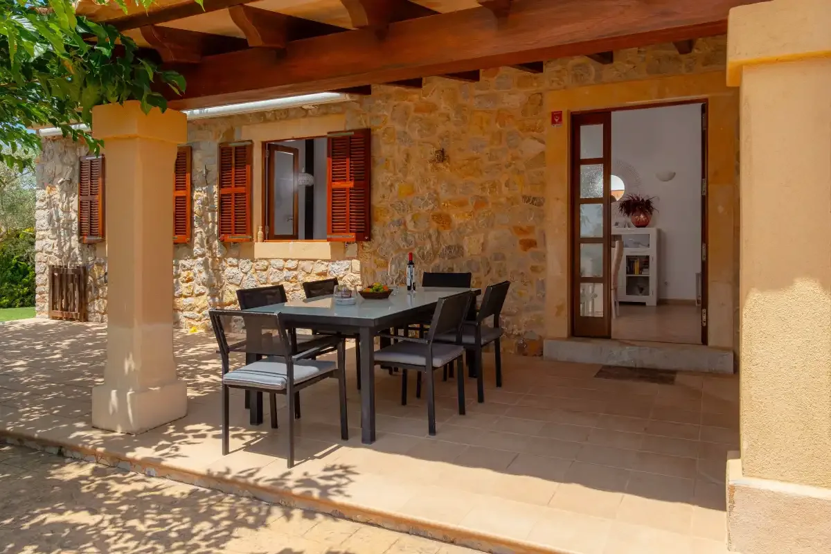 A stone-walled patio has a dining table and seating beneath a wooden roof.