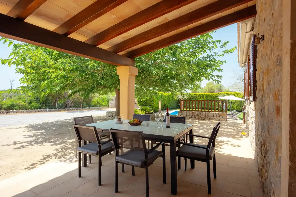 A covered outdoor dining area with a table and seating overlooks a sunny terrace.