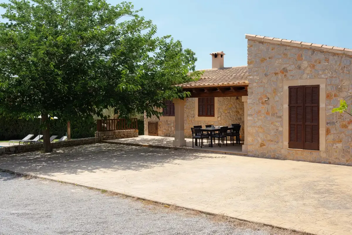 A stone house opens onto a paved patio with outdoor seating beneath a tree.