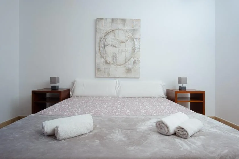 A bedroom with a large bed, white bedding, and abstract wall art.