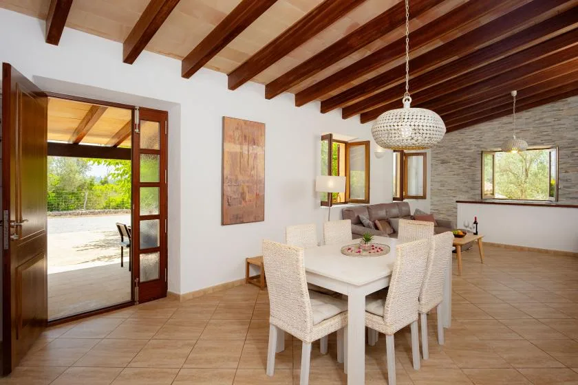 A dining and living area with a white table beneath exposed wooden ceiling beams.