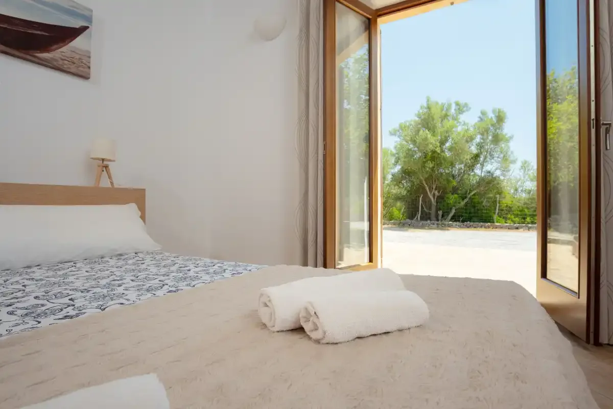 A bedroom with a bed and towels beside an open glass door.