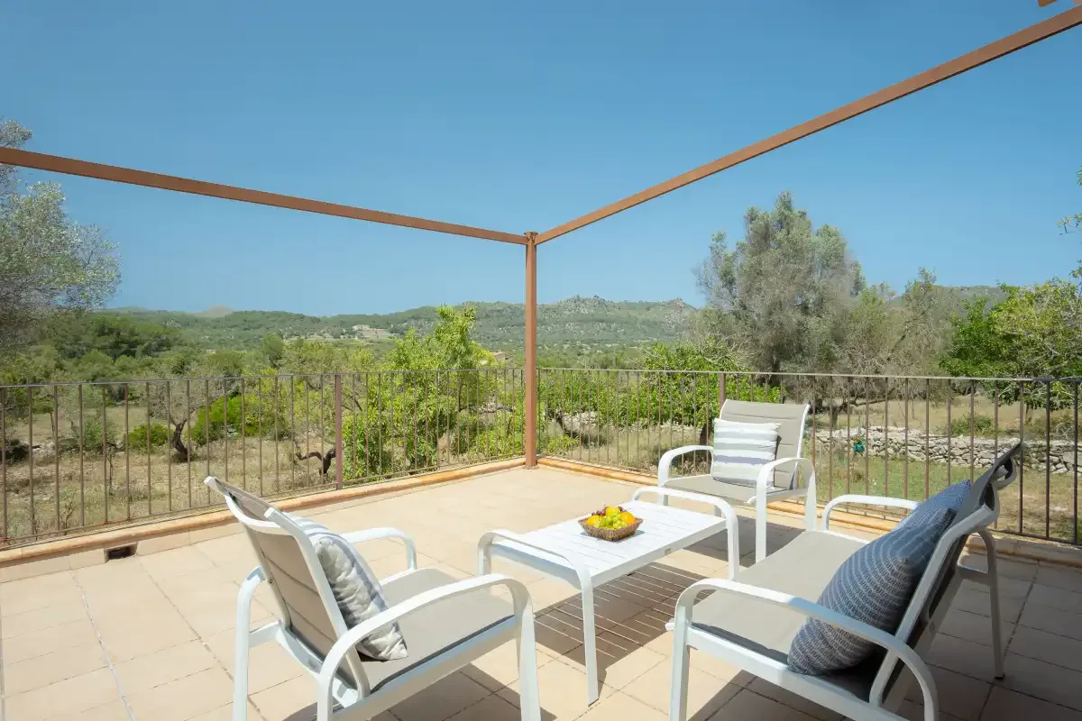 An outdoor terrace with seating and a table overlooks green hills.