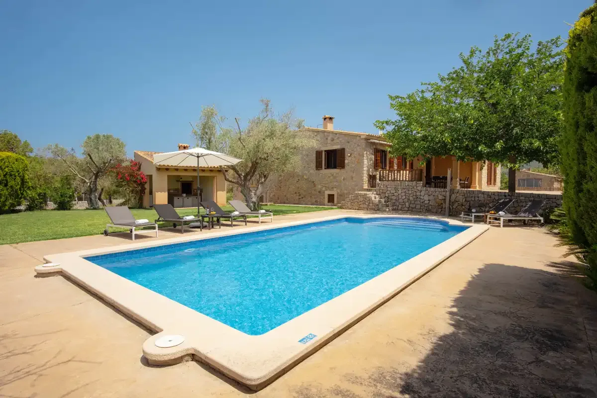 A swimming pool and sun loungers sit beside a stone house.