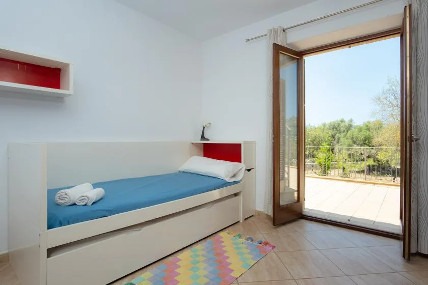 A bedroom with a single bed beside an open glass door to a balcony.
