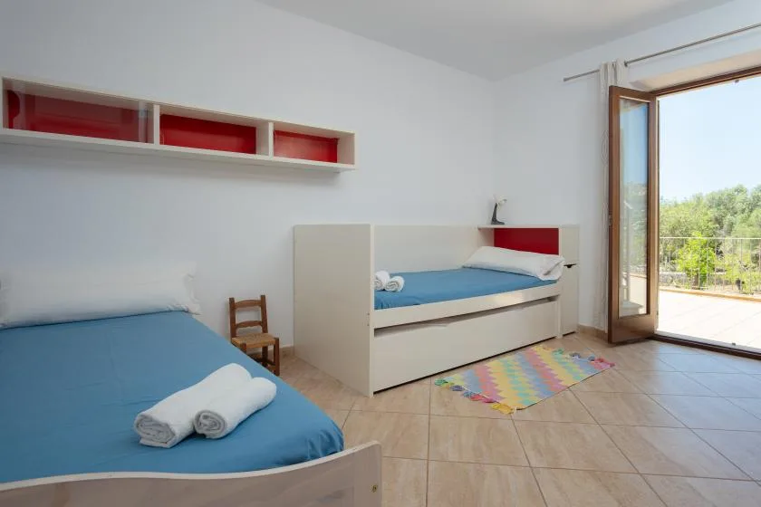 A bright bedroom with blue bedding and an open door to a balcony.