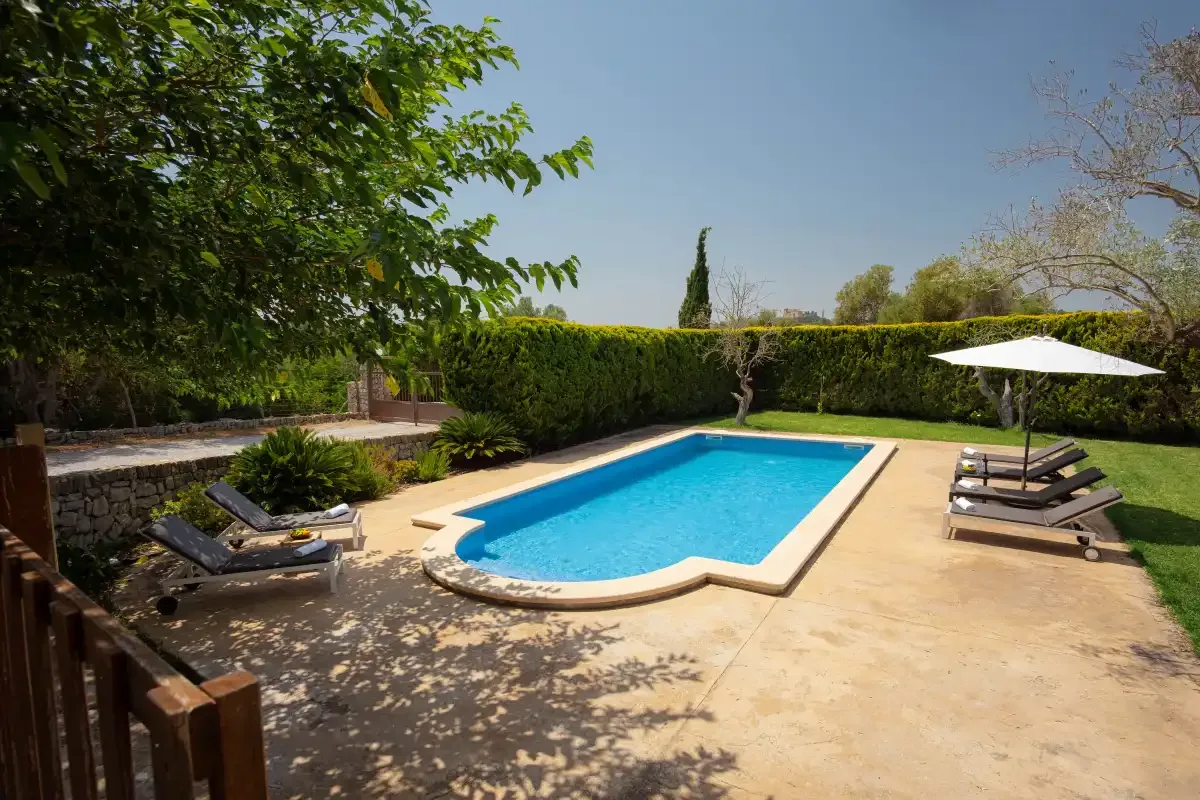 An outdoor swimming pool sits beside a paved deck and shaded lounge seating.