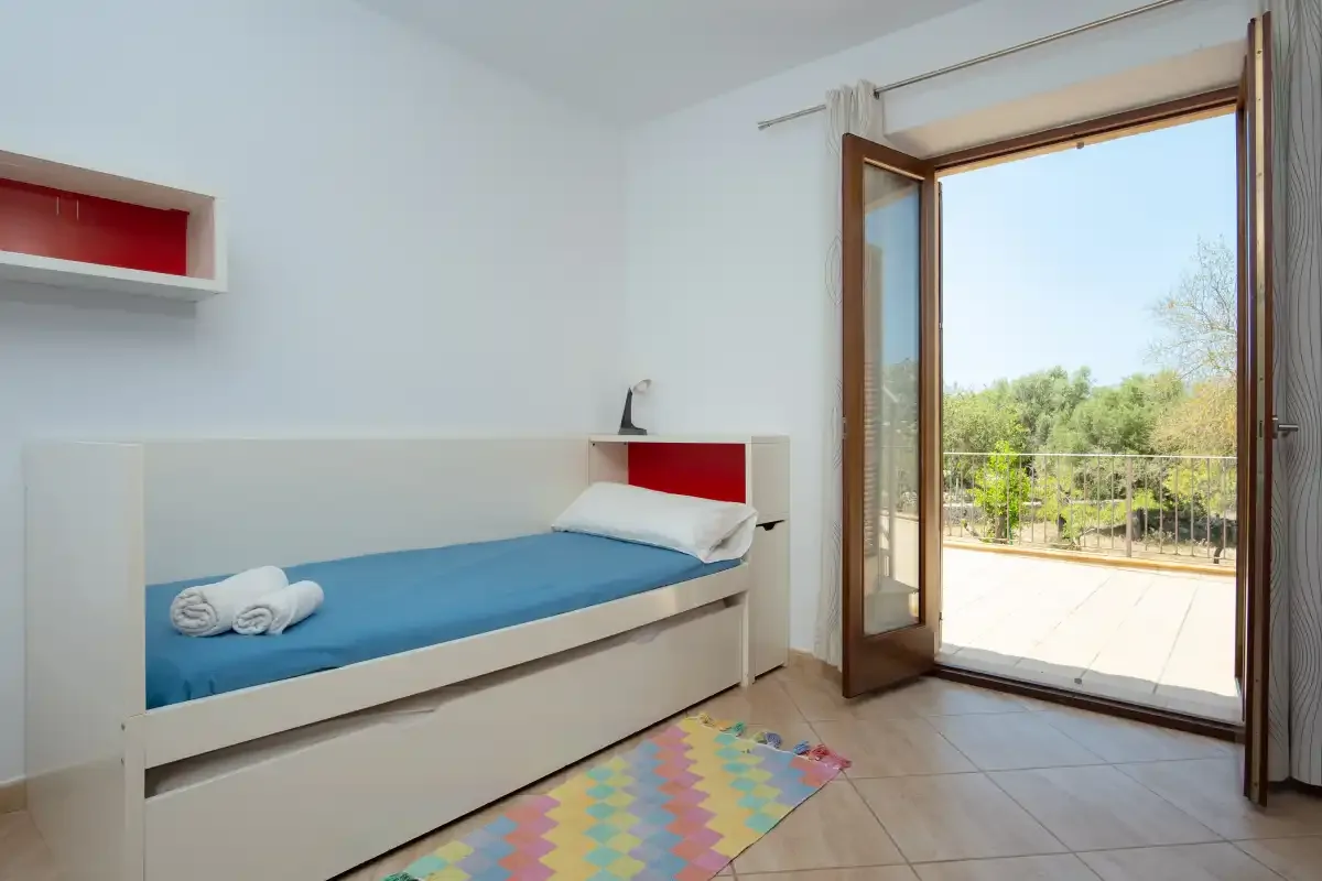 A bright bedroom with a single bed and an open door to a sunny patio.