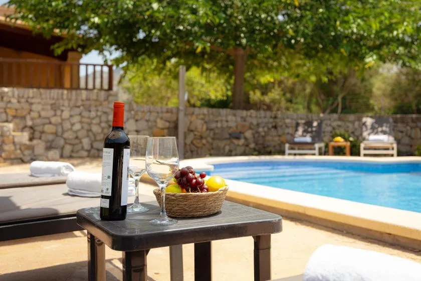 A sunny poolside patio with a table holding wine, glasses, and fruit.