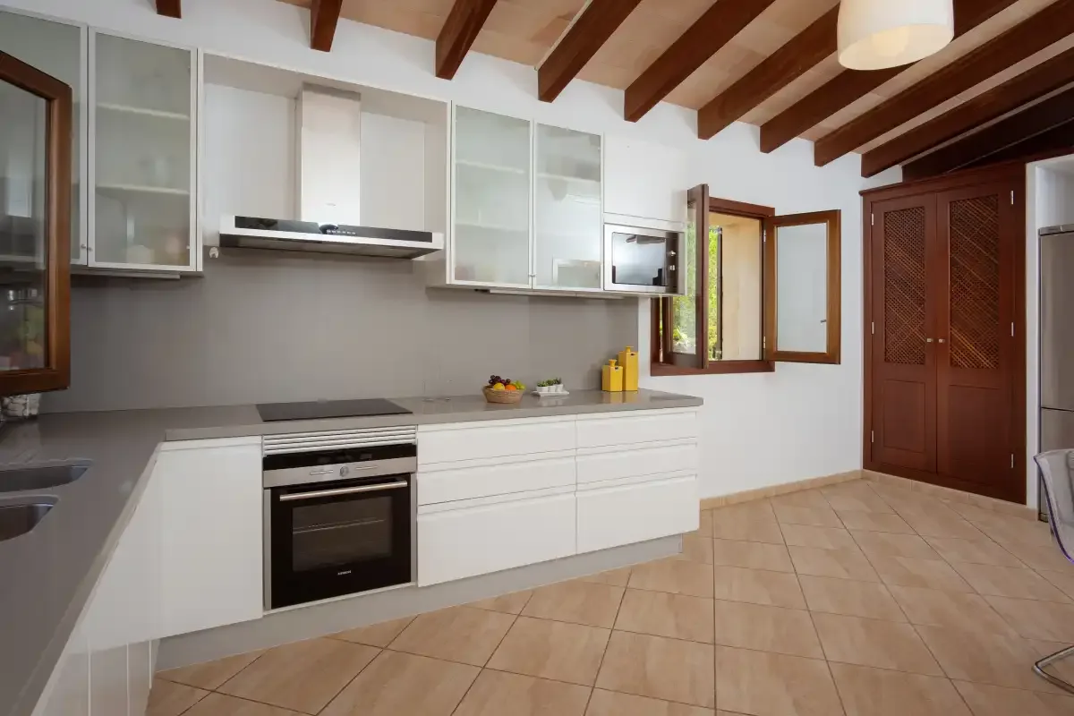 A bright kitchen with white cabinets, a built-in oven, and exposed ceiling beams.