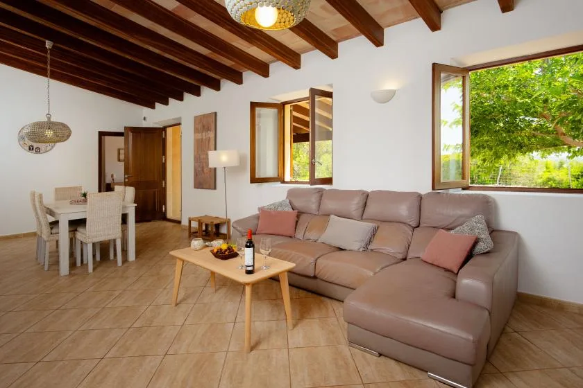 A living room with a sectional sofa and a dining table beside open windows.