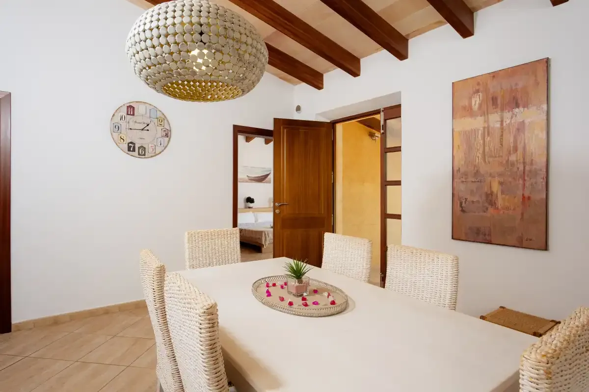 A dining room with a white table and woven seating beneath exposed wooden beams.