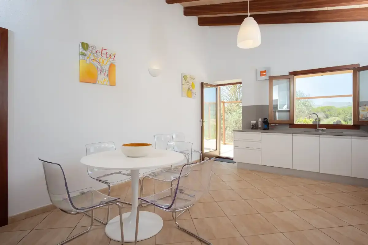 A dining area with a round table and clear chairs beside a kitchen.