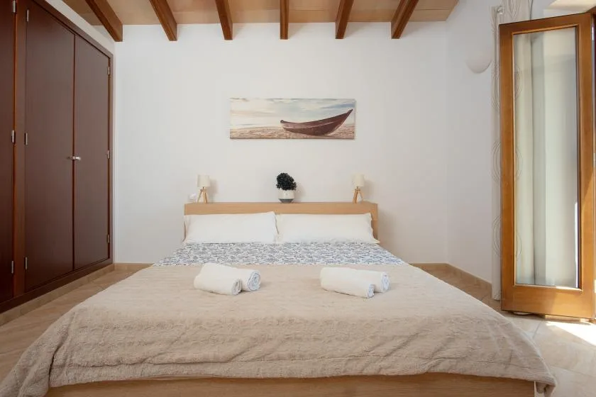 A bedroom with a neatly made bed and a framed boat picture above it.