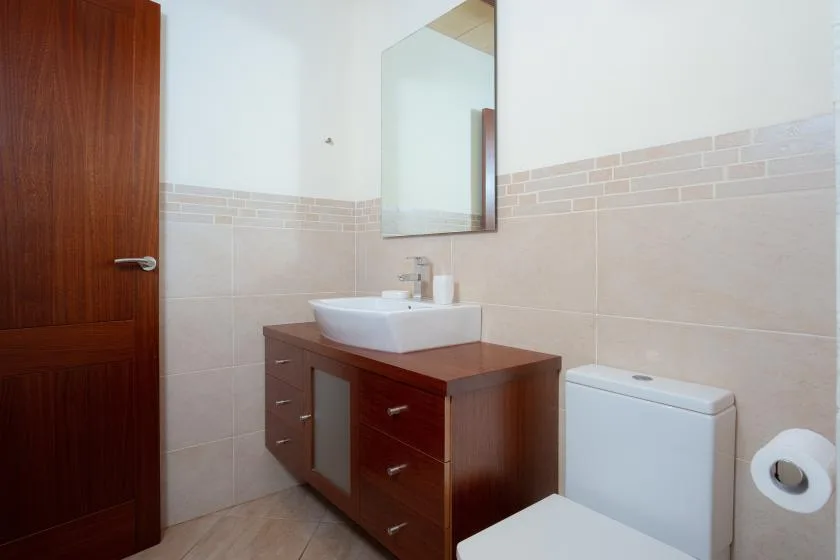 A tiled bathroom with a vanity, sink, mirror, and toilet.