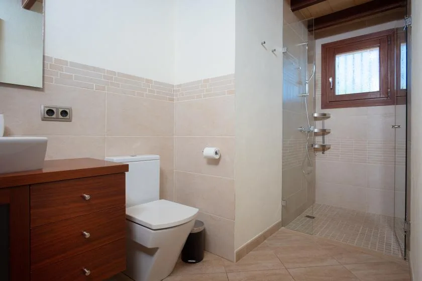 A tiled bathroom with a wooden vanity, toilet, and glass shower.