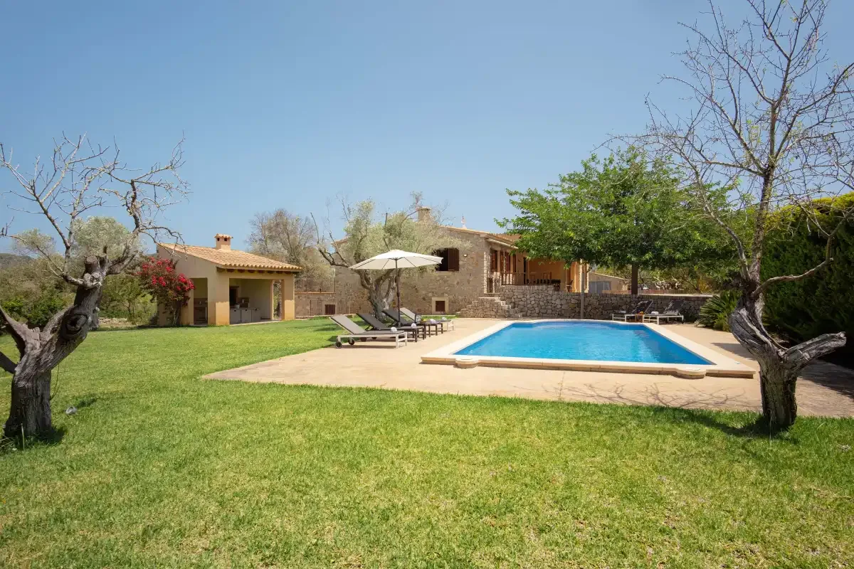 A grassy garden surrounds a swimming pool beside a stone house.