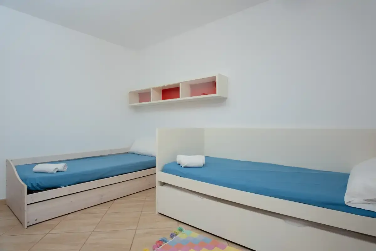 A bright bedroom with two beds and a small wall shelf.