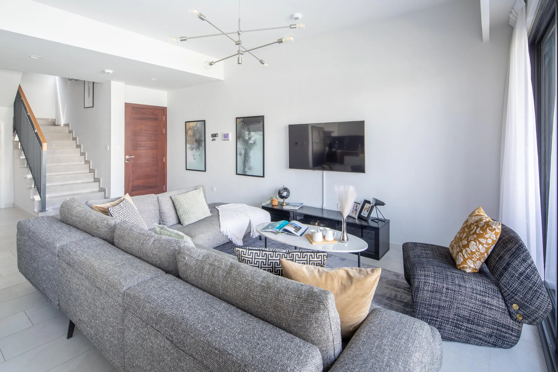 Una sala luminosa con asientos grises, una mesa de centro y un televisor en la pared.