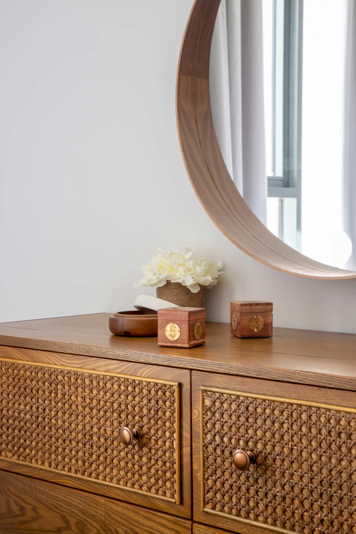 Una cómoda de madera con frentes de cajón tejidos está bajo un espejo redondo.