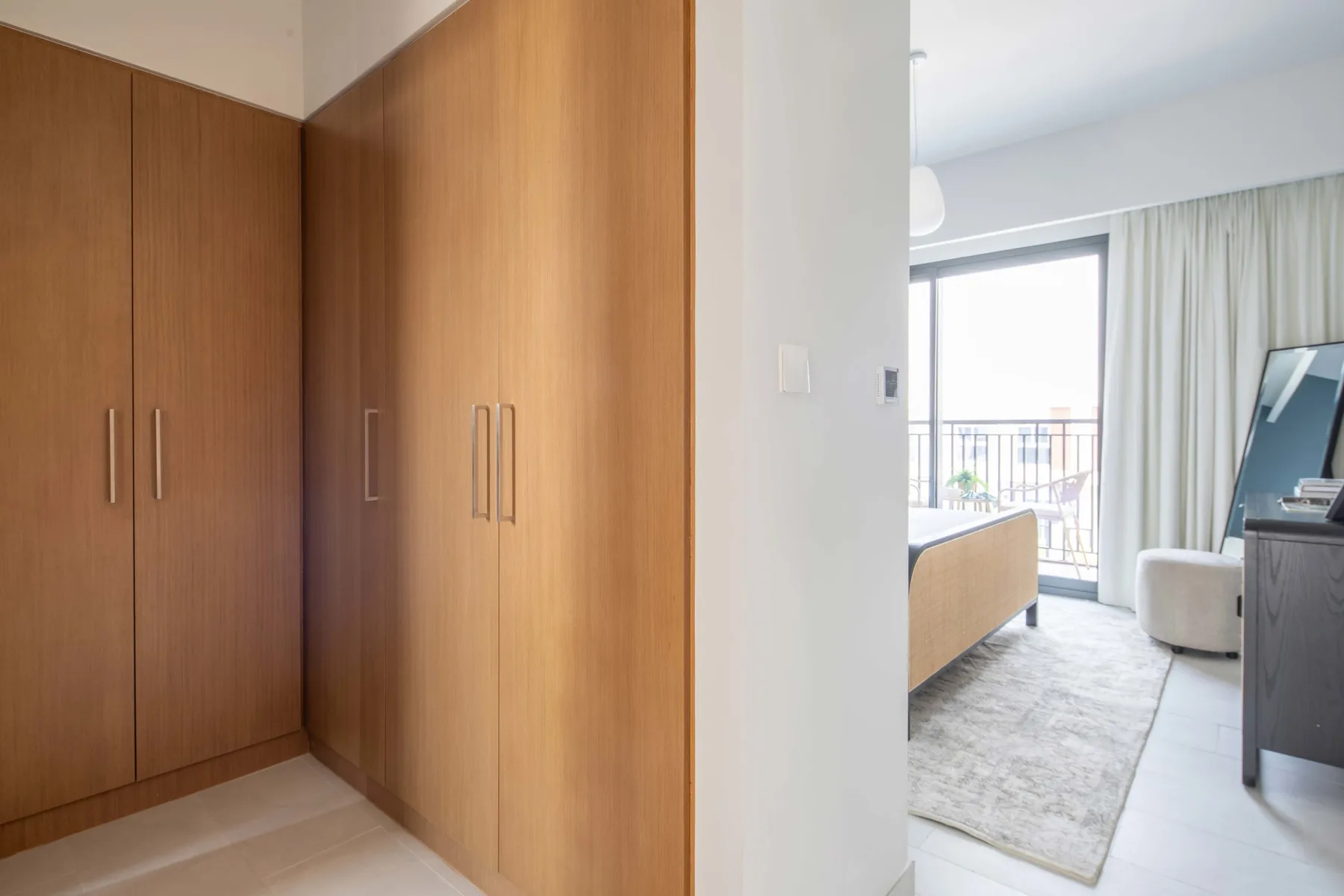 Un dormitorio luminoso con armarios de madera, una cama y una ventana con salida a un balcón.