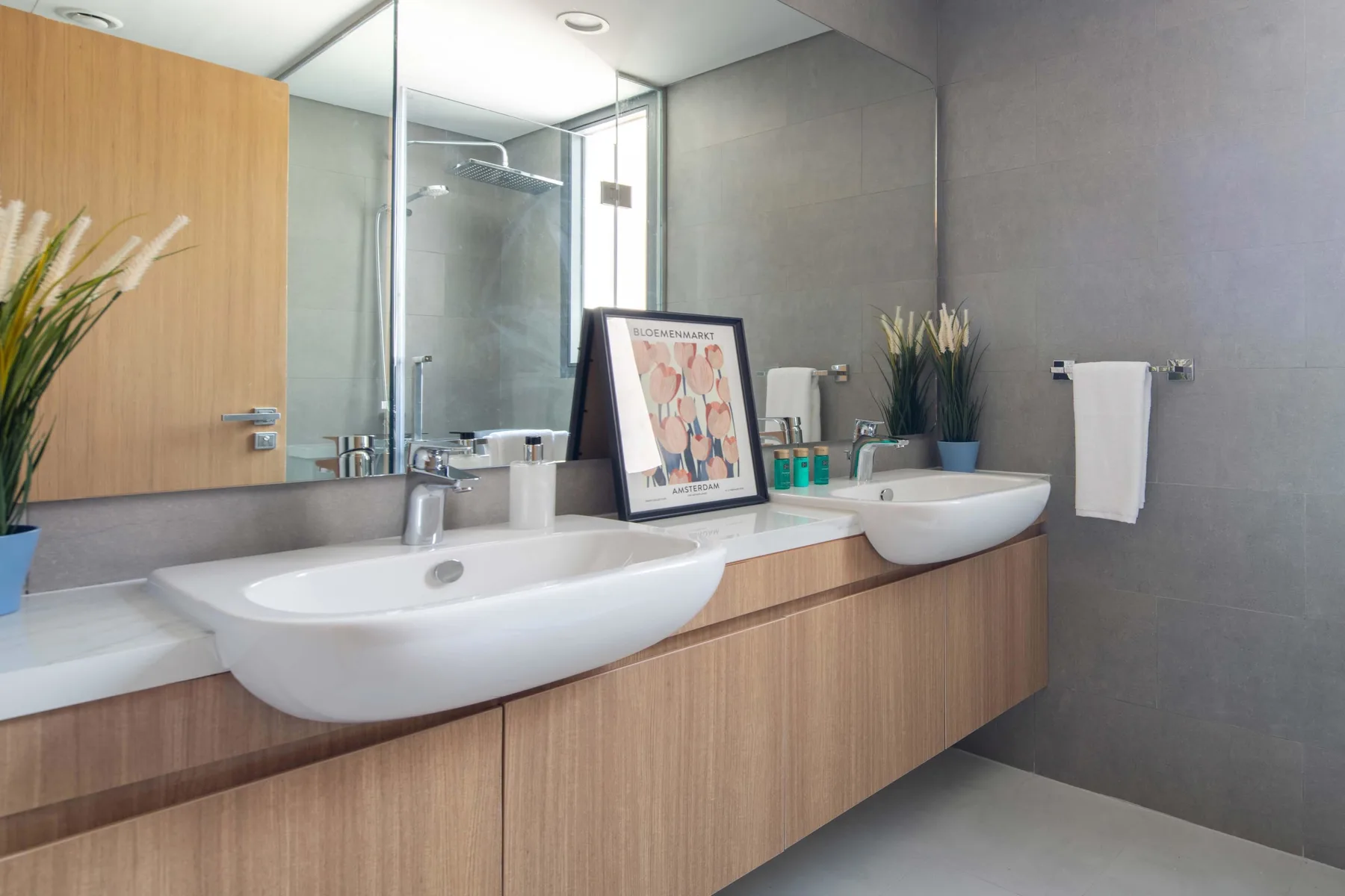 Un baño moderno con dos lavabos, un espejo grande y paredes de azulejos grises.