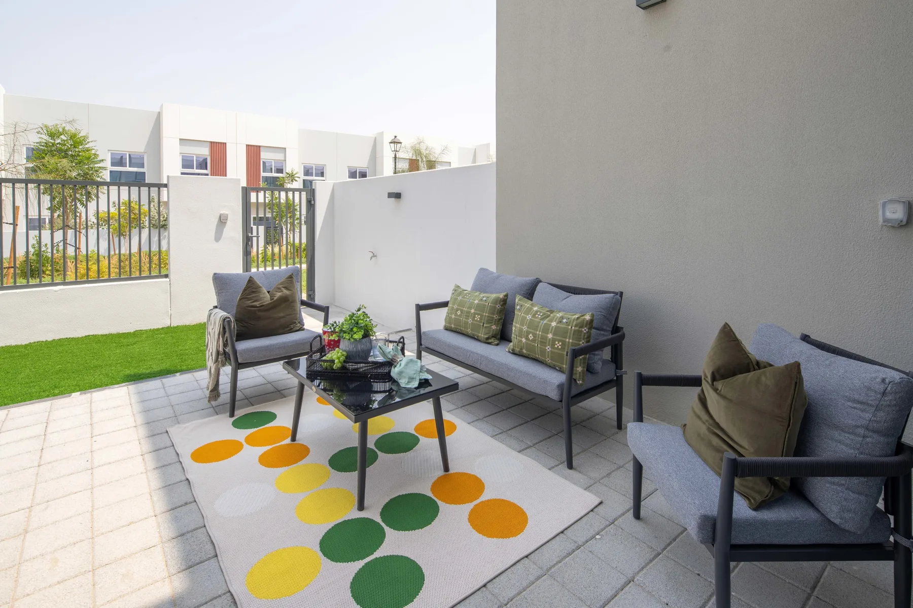 Un patio al aire libre con asientos acolchados alrededor de una mesa baja y una alfombra colorida.