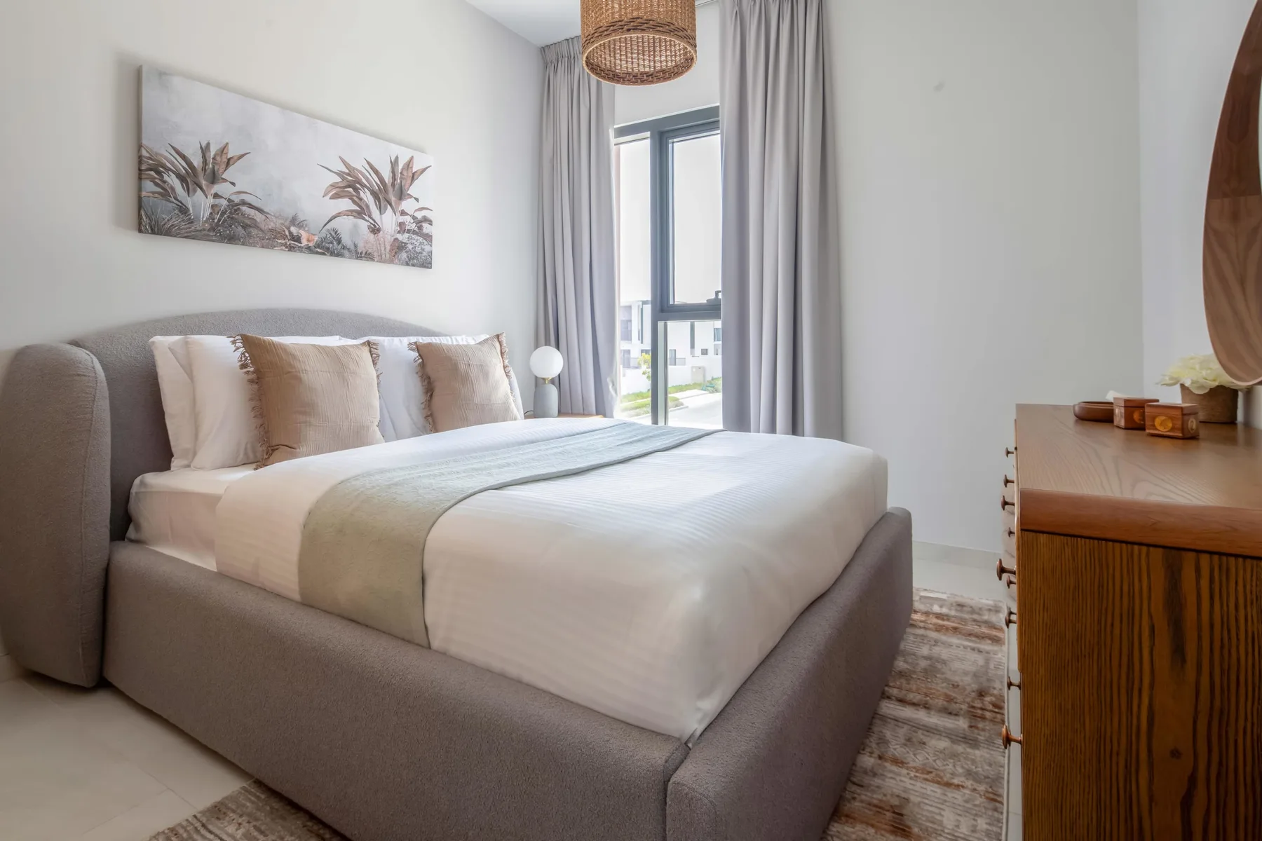 Un dormitorio con una cama bien tendida junto a una ventana alta con cortinas.