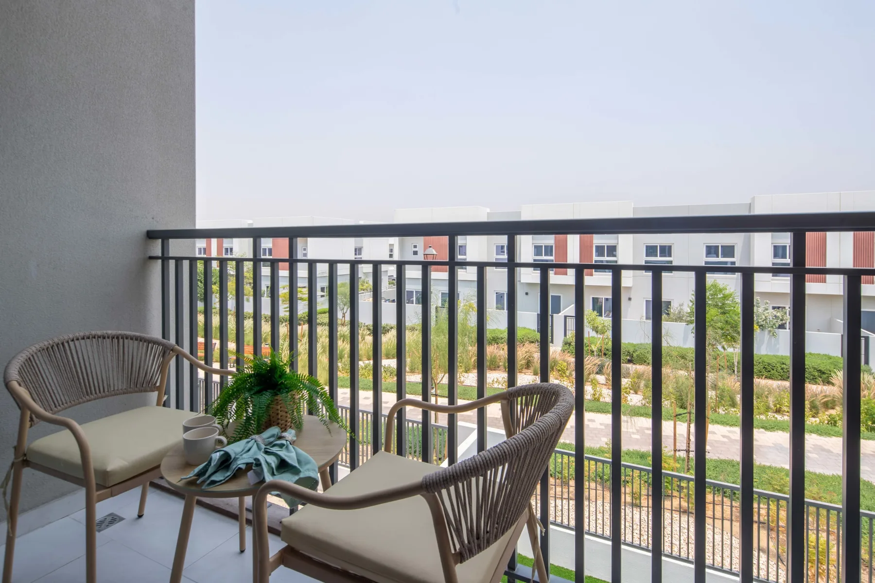 Una zona de estar en el balcón da a vegetación y edificios de apartamentos cercanos.