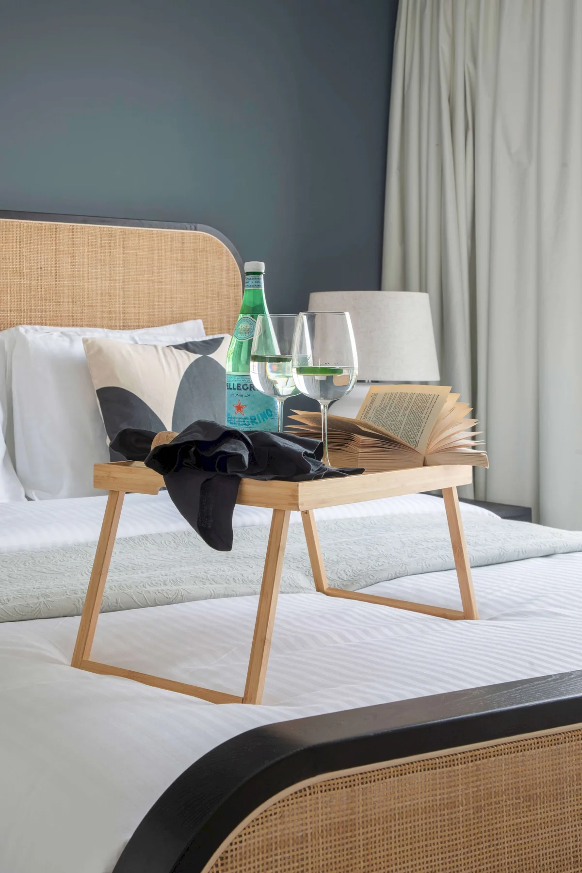 Un dormitorio con una cama y una bandeja pequeña con bebidas y un libro abierto.
