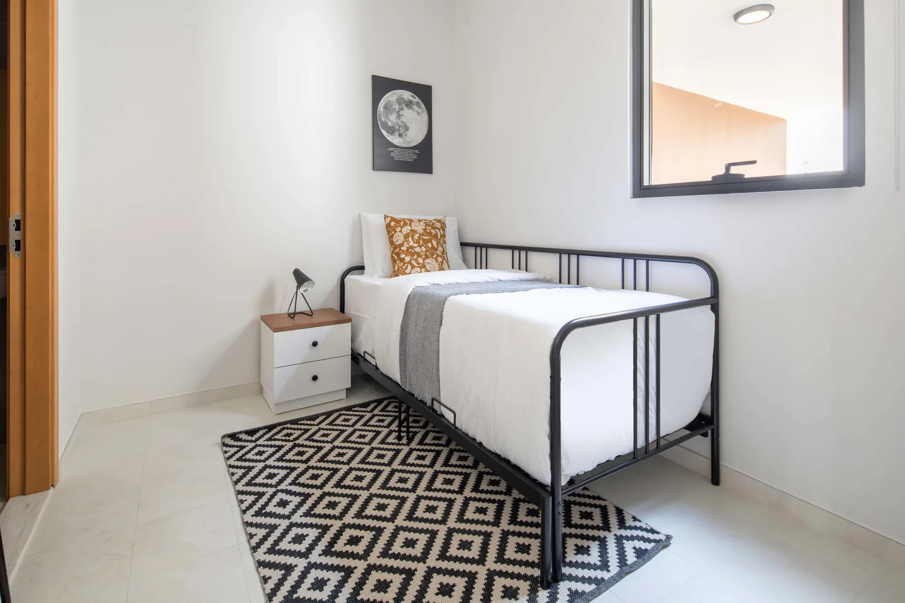 Un dormitorio con una cama individual, una mesita de noche y una alfombra estampada.