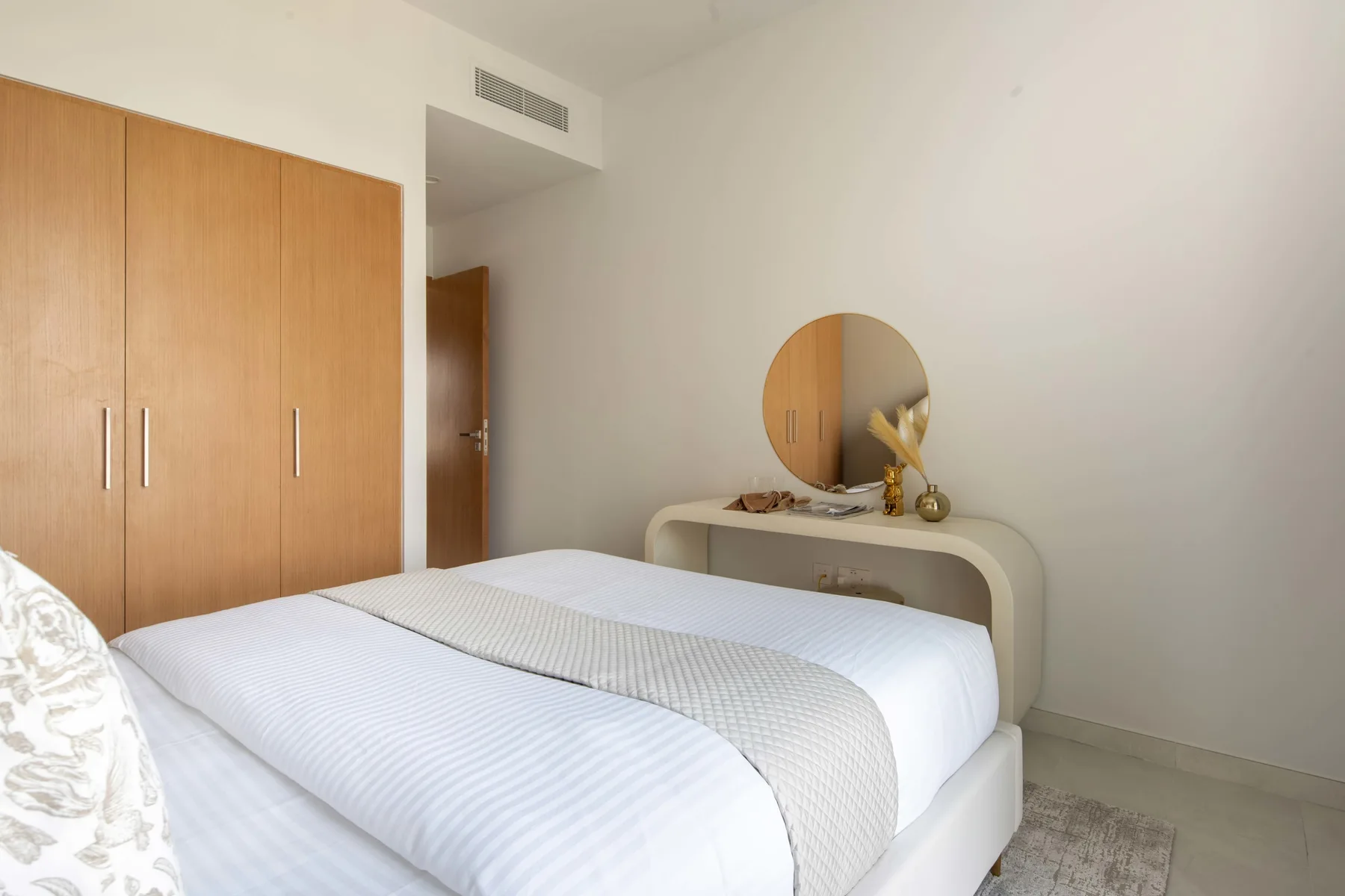 Un dormitorio luminoso con una cama bien hecha y un armario de madera.