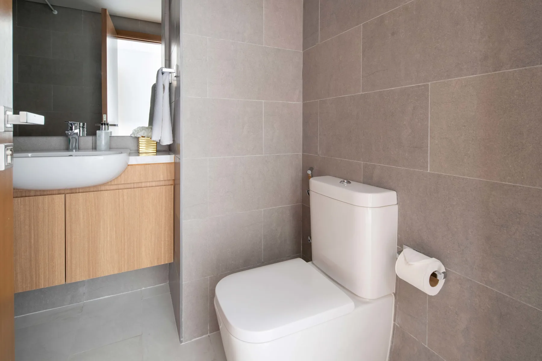 Baño con un inodoro junto a un lavabo y un mueble de frente de madera.