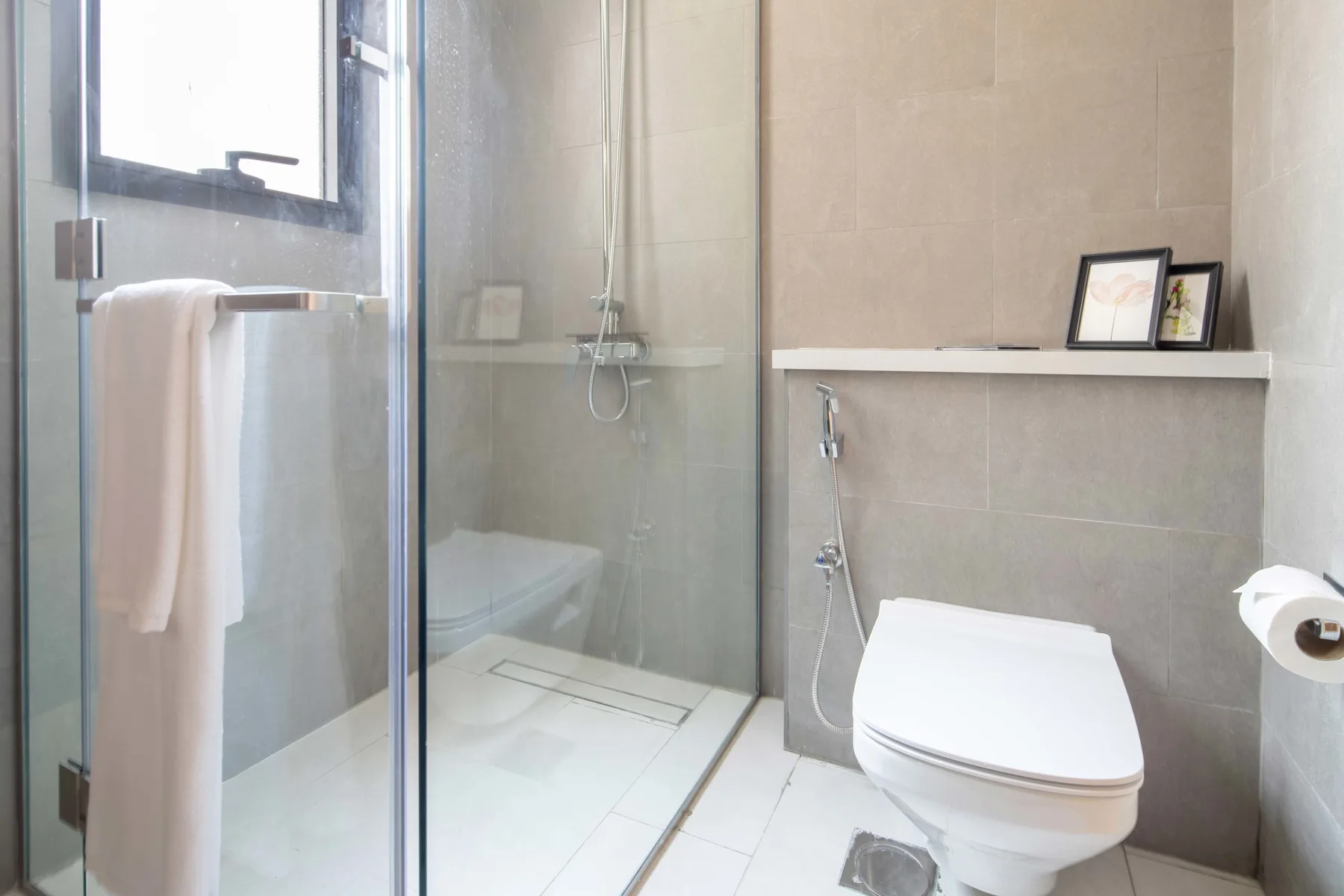 Un baño con ducha de vidrio, inodoro y una toalla colgada junto a la ventana.