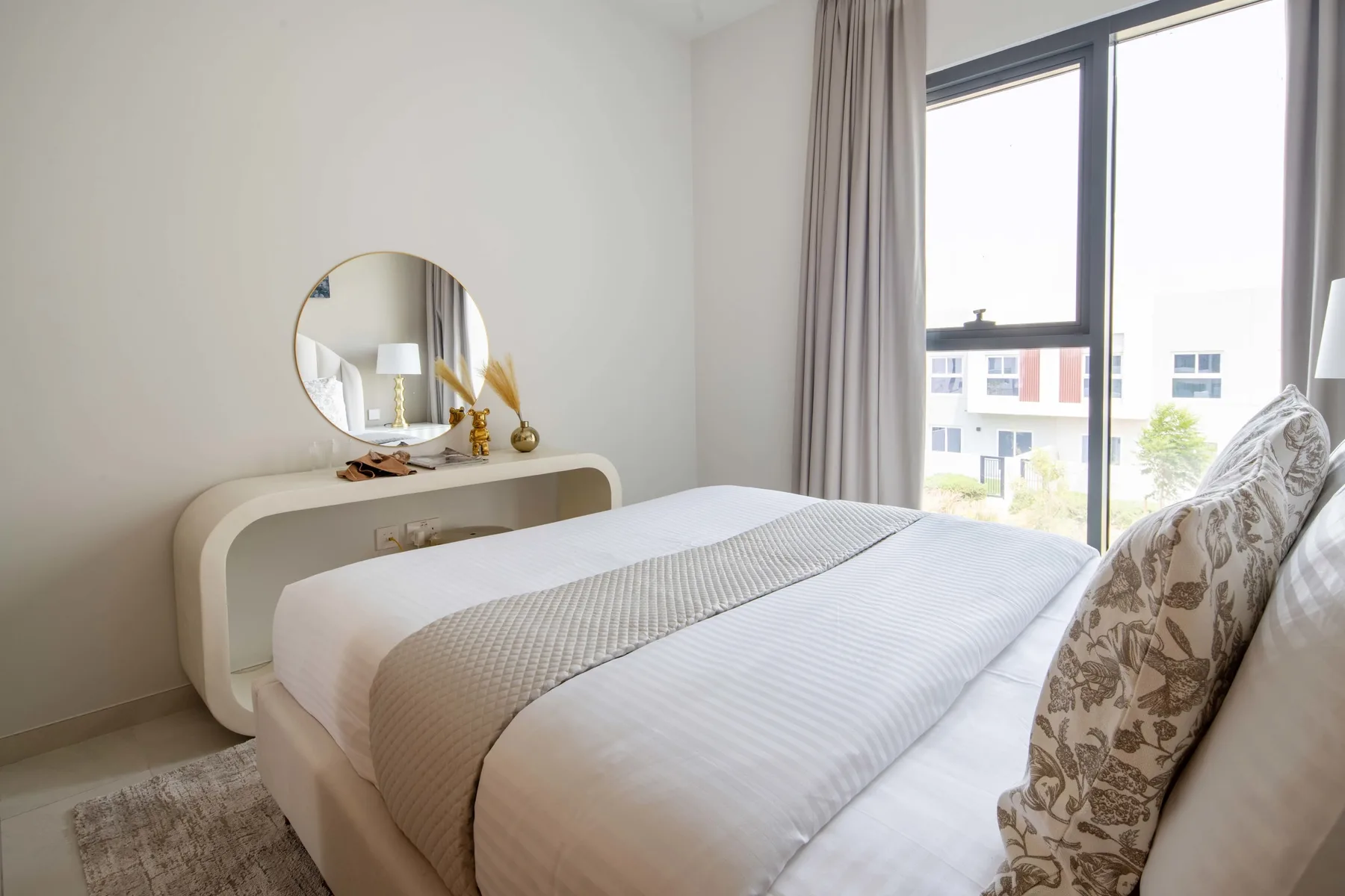 Un dormitorio luminoso con una cama bien tendida junto a una ventana grande.