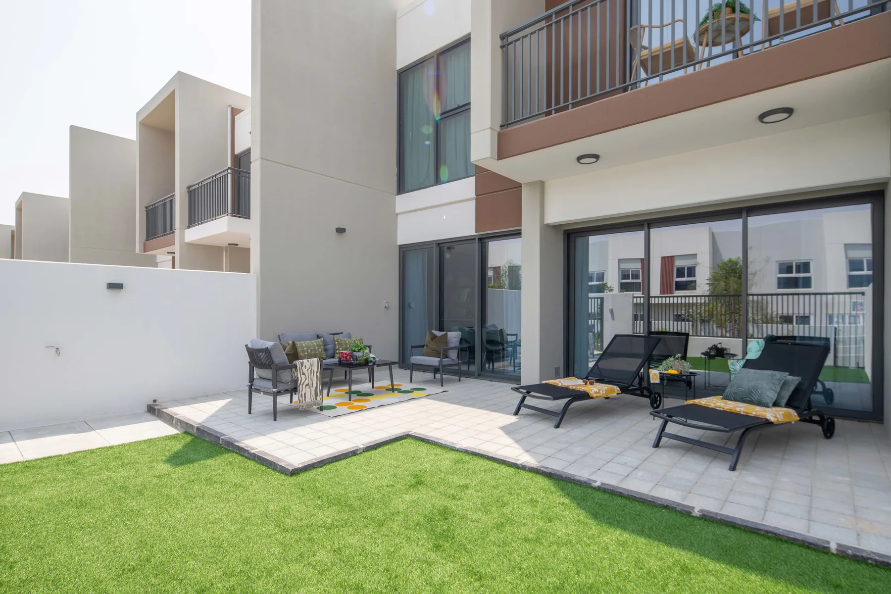 Un patio pavimentado con asientos y tumbonas junto a un césped.