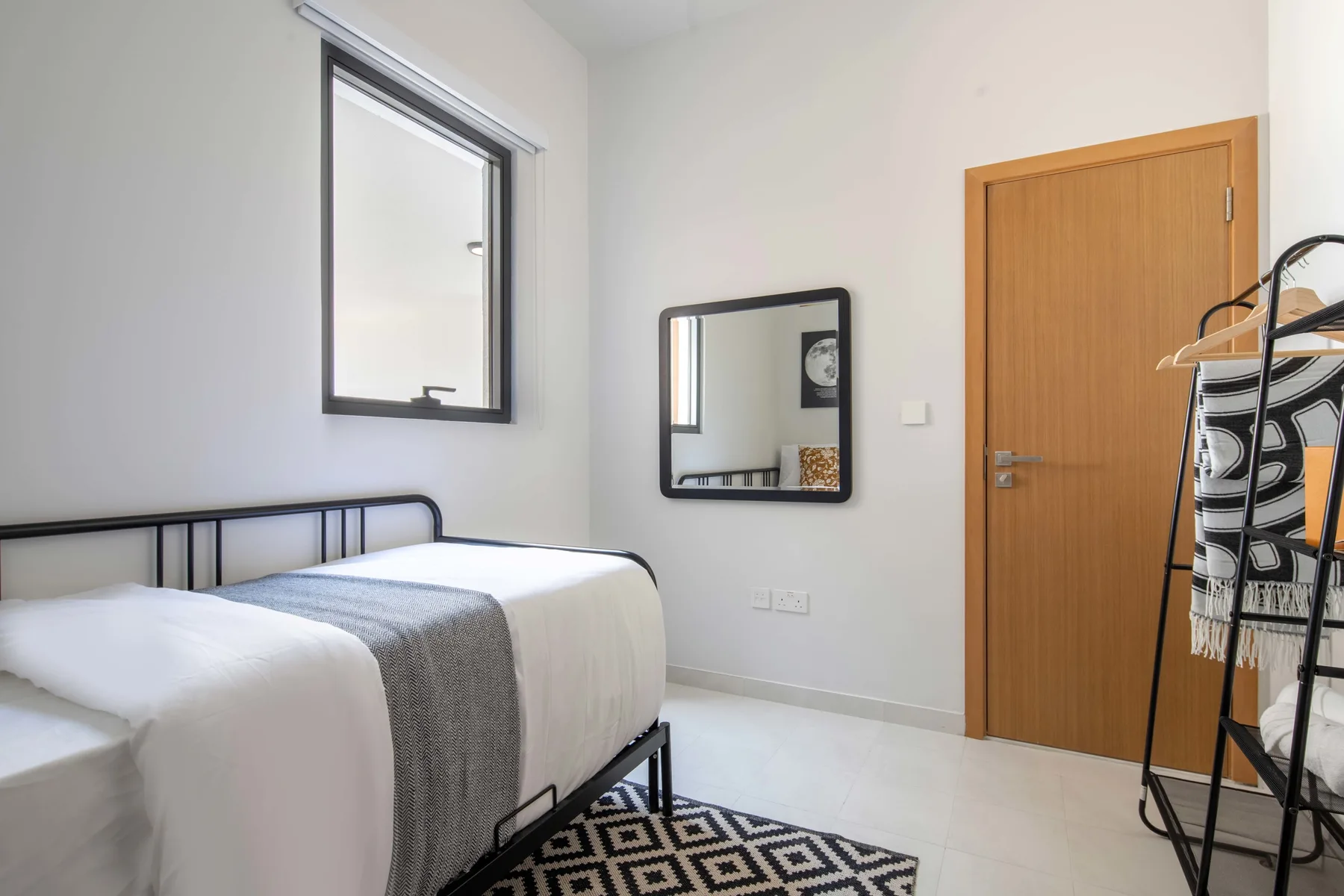 Un dormitorio con una cama bien tendida, un espejo de pared y una puerta de madera.