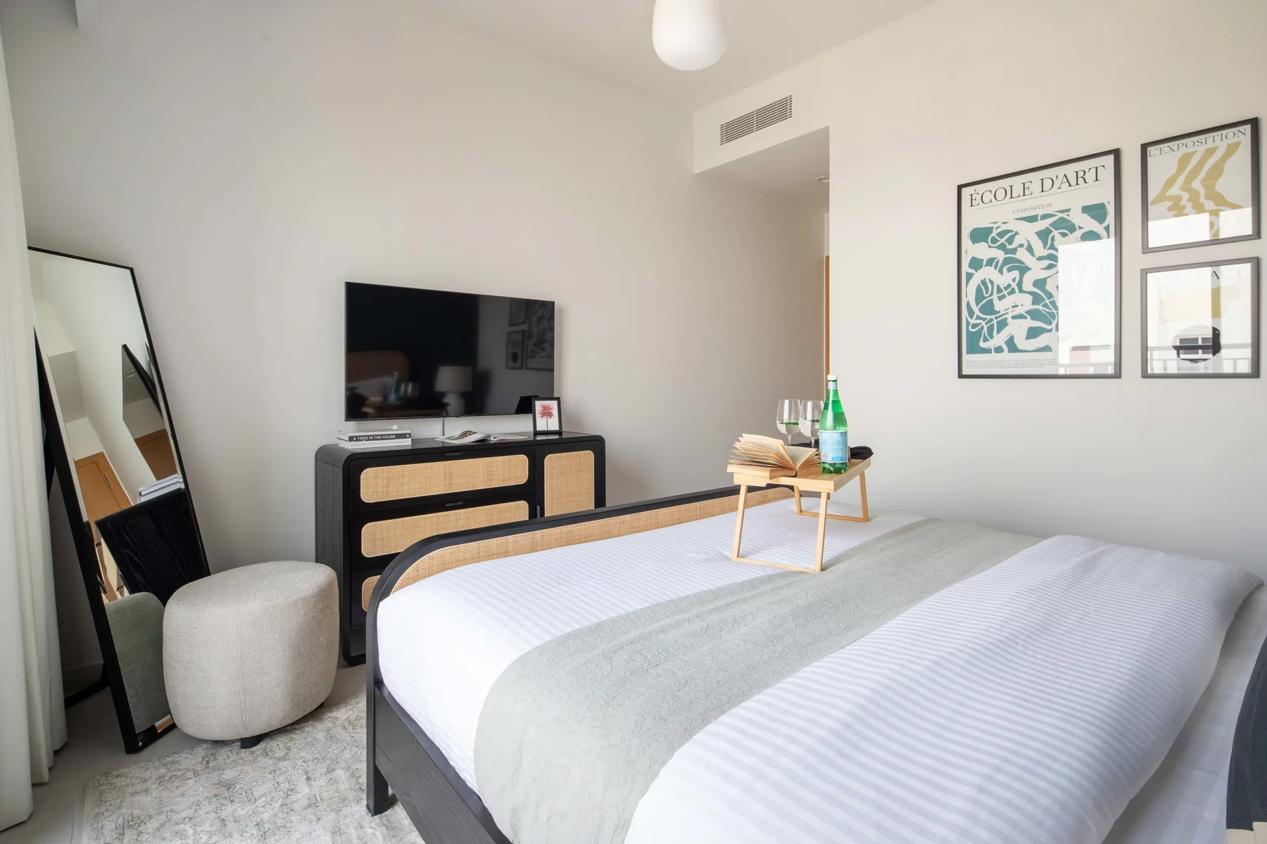 Un dormitorio luminoso con una cama, un televisor y cuadros enmarcados.