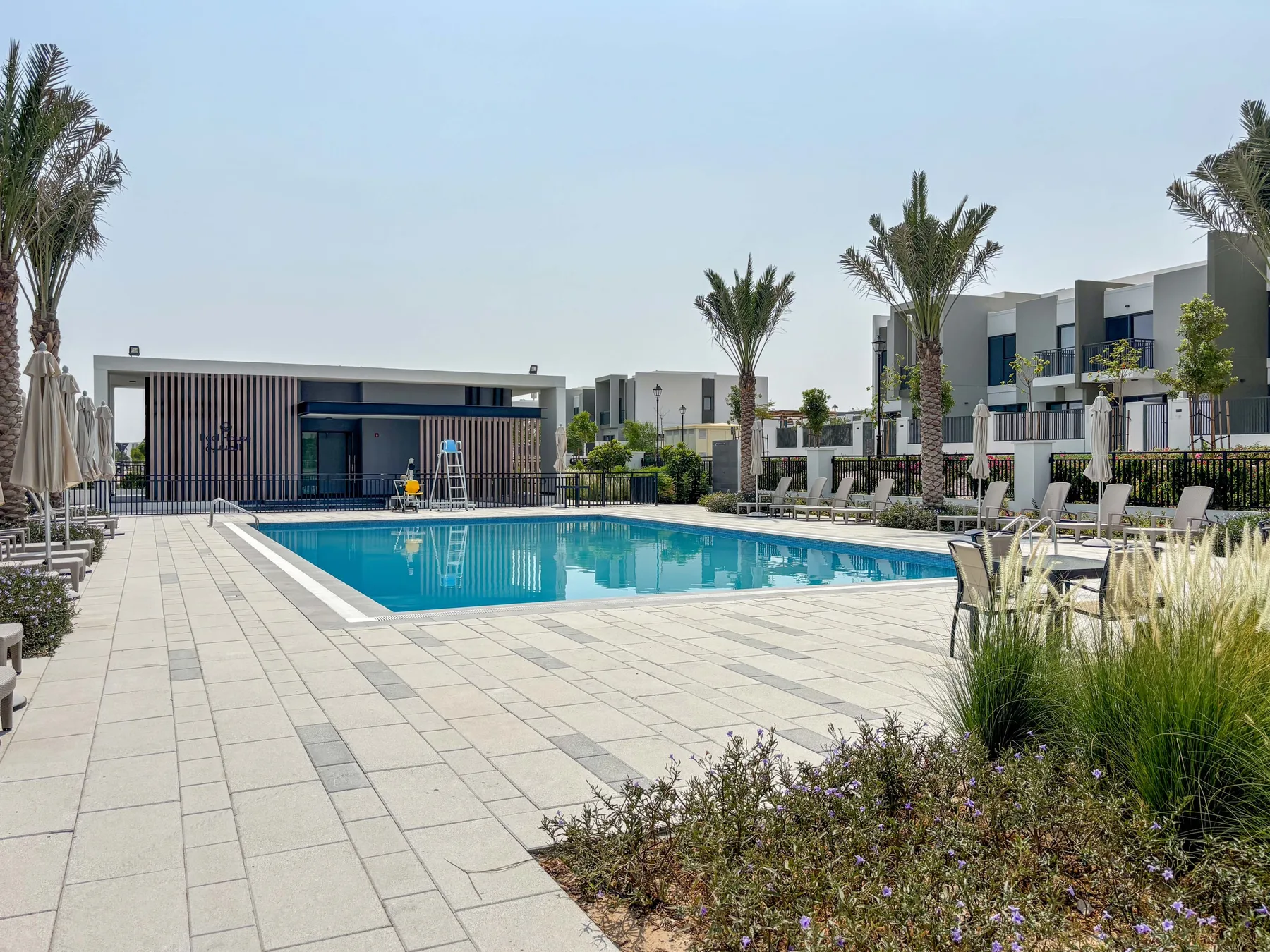 Una piscina al aire libre está junto a una terraza pavimentada y jardines.
