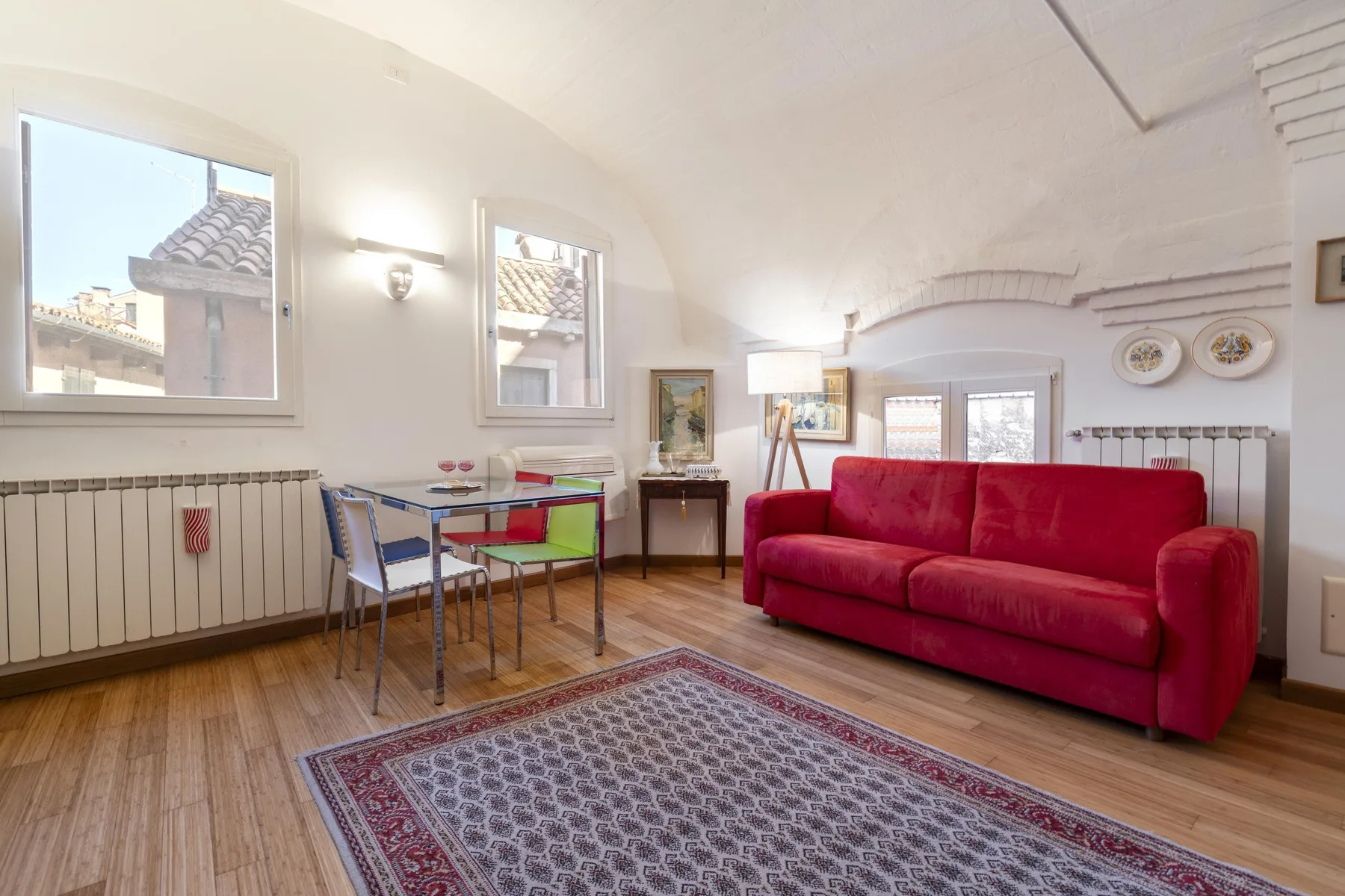 Una sala luminosa con asientos rojos, una mesa de comedor y una alfombra estampada.