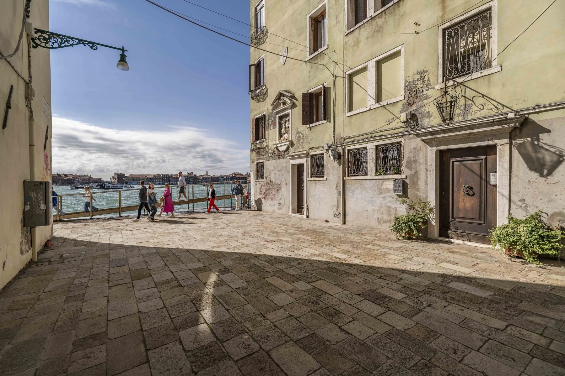 A paved waterfront square beside an old building, with people near the railing.