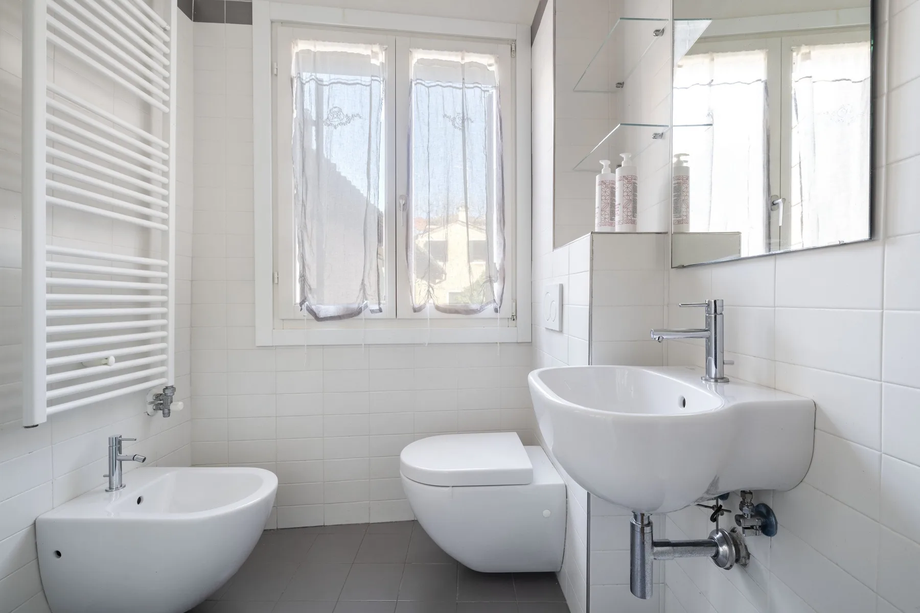A tiled bathroom with a bathtub, toilet, and sink beneath a mirrored cabinet.
